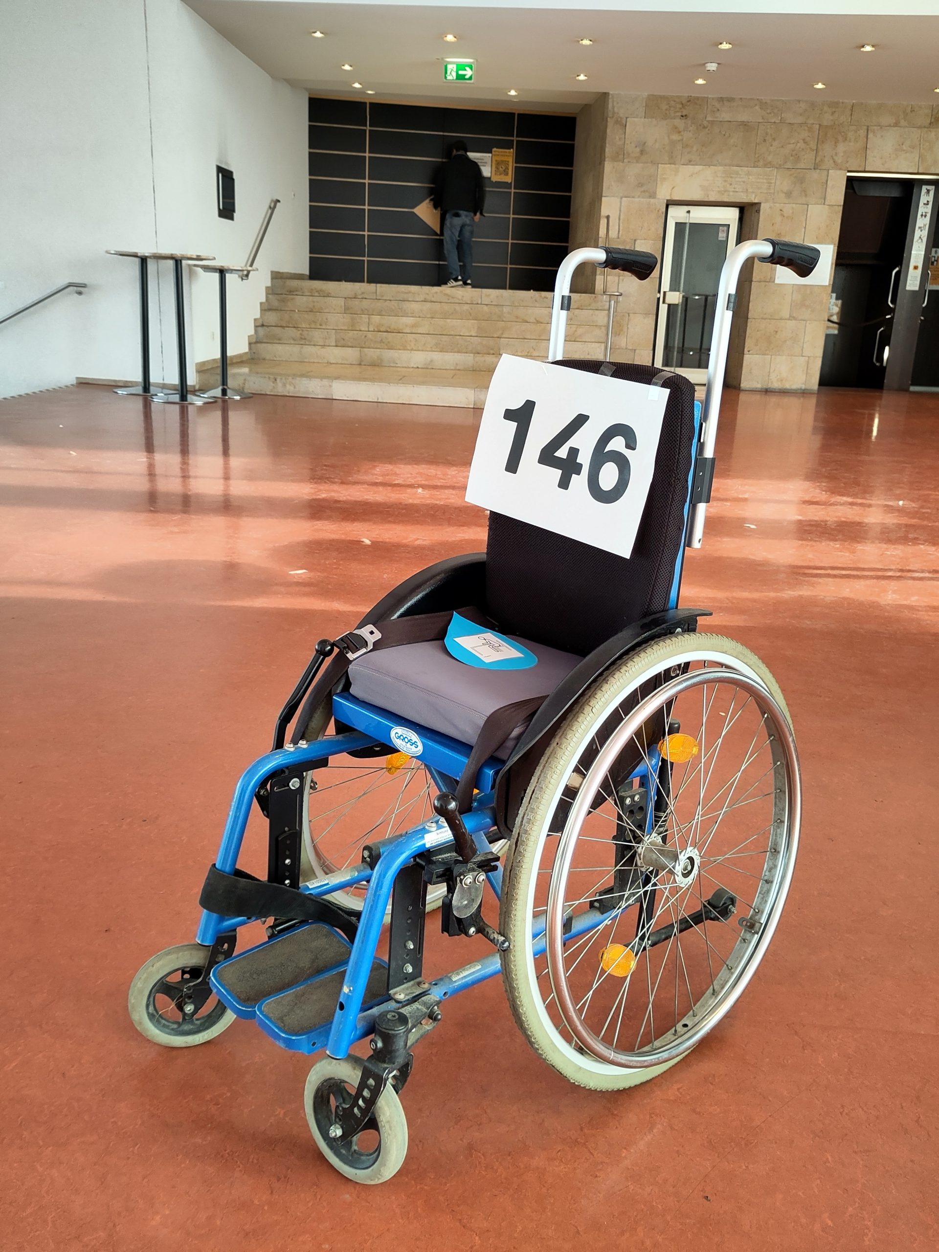 Ein Rollstuhl steht im Flur vor dem Sitzungssaal im Stuttgarter Rathaus. Auf der Lehne klebt ein Schild mit der Zahl "146". Die Zahl steht für die Anzahl der Kinder mit Behinderungen, die über Nacht ohne Schulbegleitung sind.